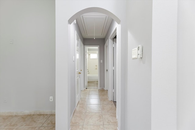 corridor with light tile patterned floors, arched walkways, attic access, and baseboards