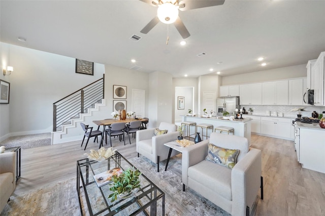 living area with light wood-type flooring, visible vents, stairway, and baseboards