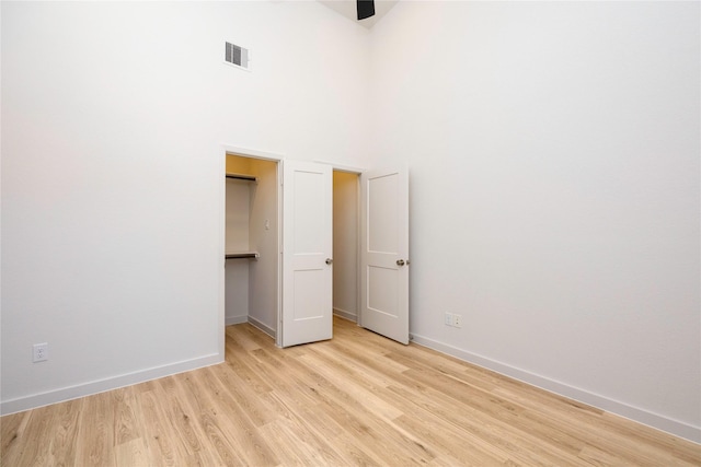 unfurnished bedroom with light wood finished floors, baseboards, visible vents, a towering ceiling, and a spacious closet