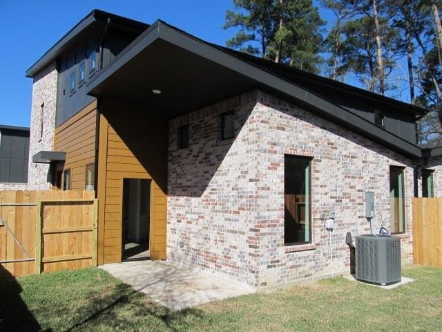 rear view of house with brick siding, cooling unit, and fence