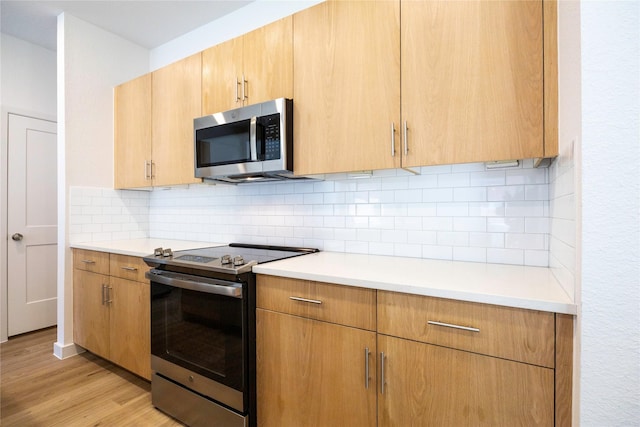 kitchen featuring stainless steel appliances, backsplash, light countertops, and light wood-style flooring