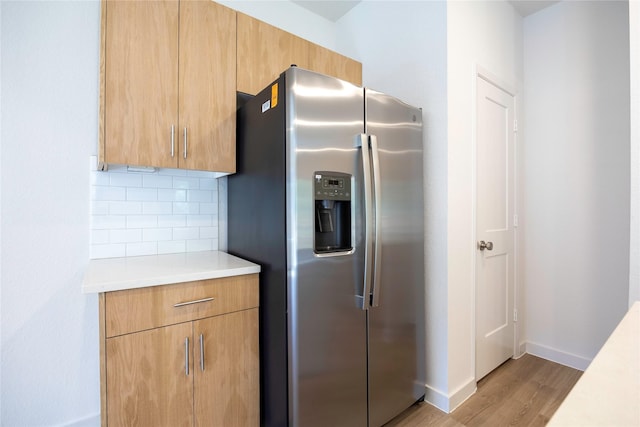 kitchen with light wood finished floors, light countertops, decorative backsplash, stainless steel fridge, and baseboards