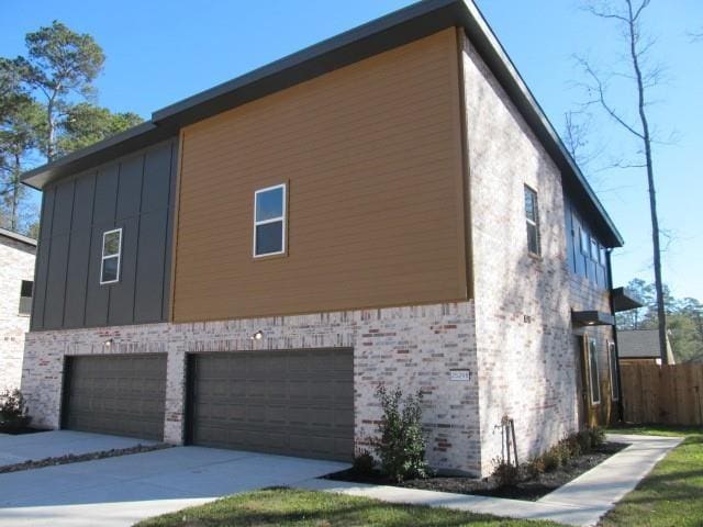 view of home's exterior with an attached garage, brick siding, fence, driveway, and board and batten siding