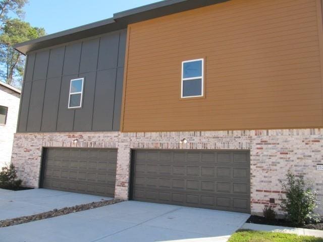 view of side of property with board and batten siding, brick siding, driveway, and a garage