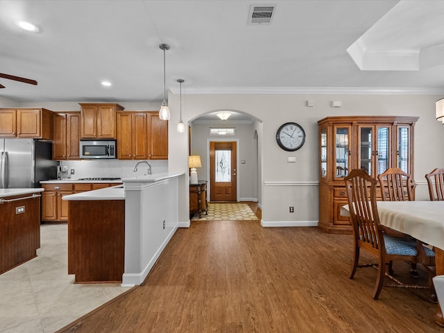 kitchen featuring visible vents, arched walkways, light countertops, appliances with stainless steel finishes, and brown cabinets