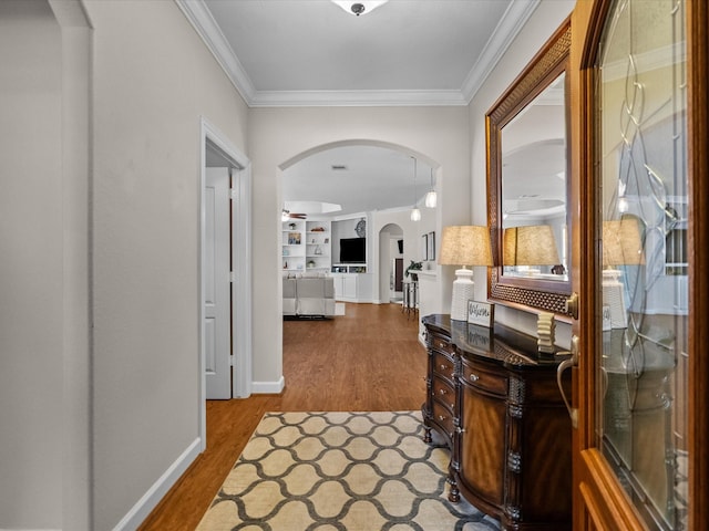 corridor with crown molding, wood finished floors, arched walkways, and baseboards