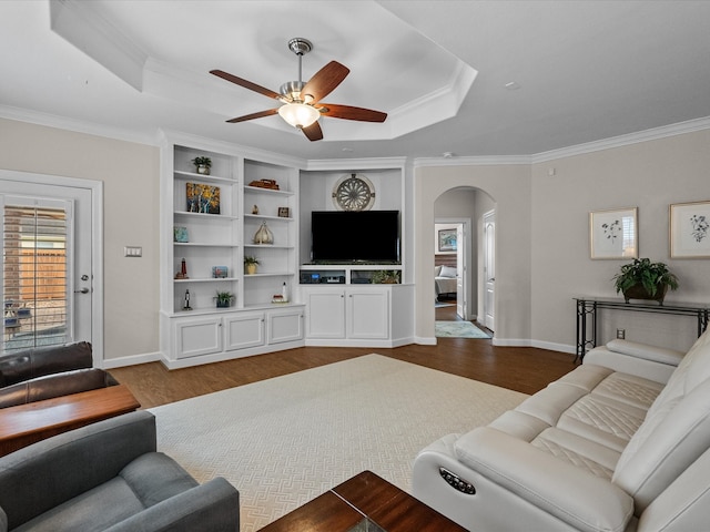 living room with dark wood-style floors, arched walkways, ceiling fan, crown molding, and a raised ceiling