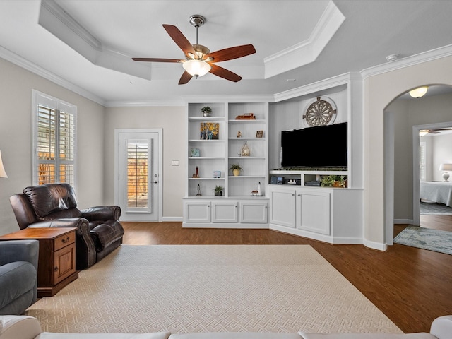 living room featuring a tray ceiling, wood finished floors, arched walkways, and ornamental molding