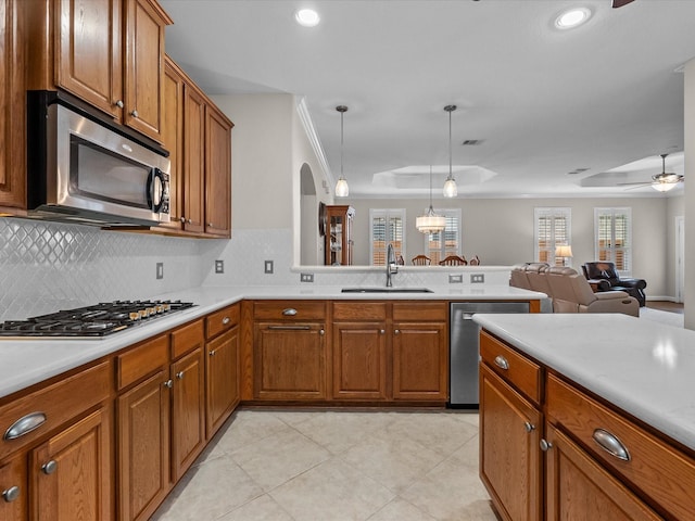 kitchen with a sink, tasteful backsplash, appliances with stainless steel finishes, brown cabinetry, and light countertops