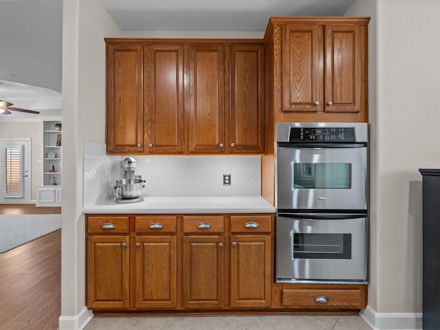 kitchen with double oven, light countertops, brown cabinets, and ceiling fan