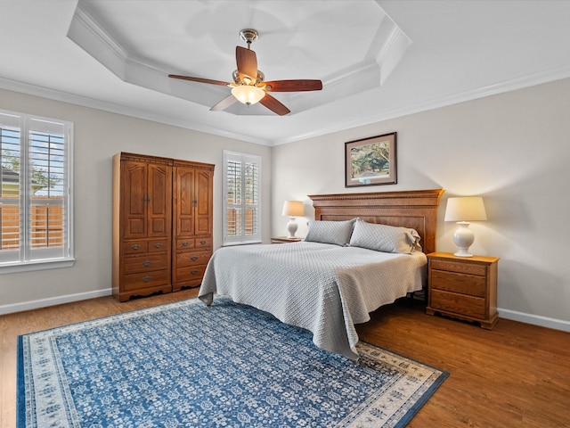 bedroom featuring multiple windows, light wood-style floors, a tray ceiling, and ornamental molding