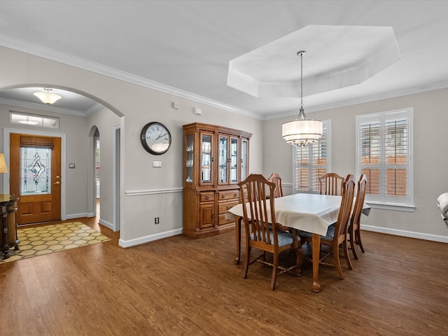 dining space with a tray ceiling, wood finished floors, arched walkways, and baseboards