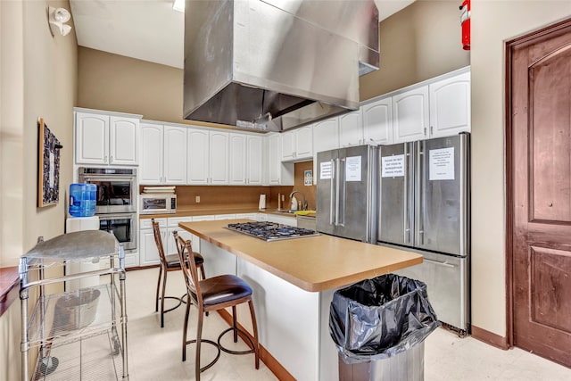 kitchen with a kitchen breakfast bar, a center island, white cabinetry, appliances with stainless steel finishes, and wall chimney exhaust hood