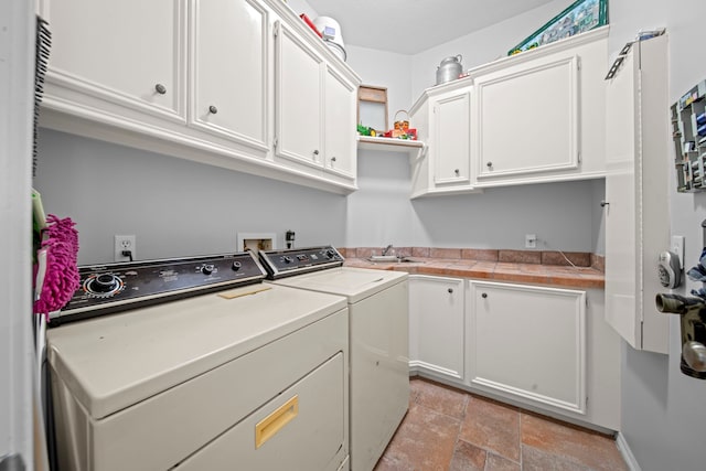 clothes washing area with washer and clothes dryer, cabinet space, stone finish flooring, and a sink