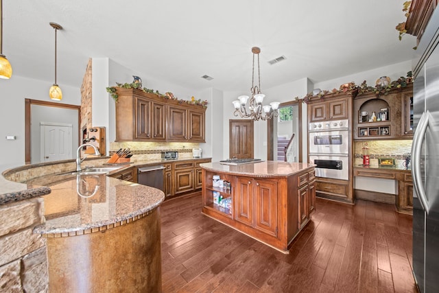 kitchen with light stone countertops, decorative backsplash, appliances with stainless steel finishes, brown cabinetry, and open shelves