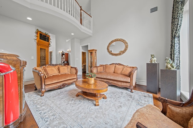 living room featuring visible vents, baseboards, a high ceiling, and wood finished floors