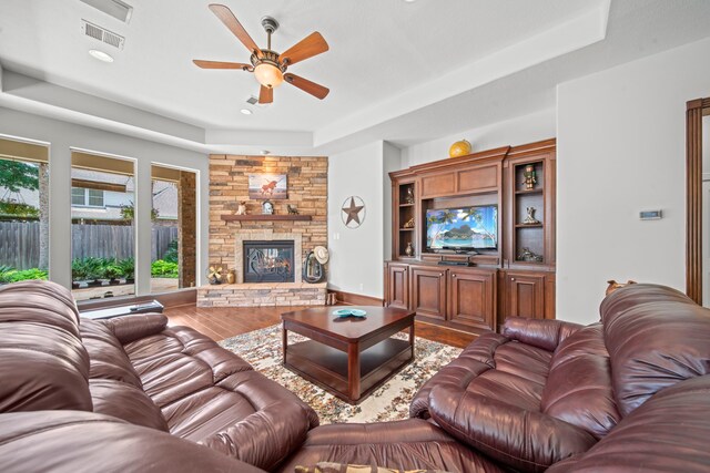 living room featuring a fireplace, a tray ceiling, wood finished floors, and visible vents