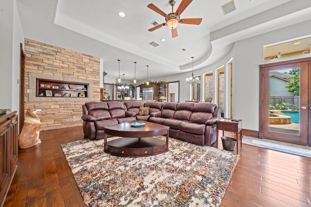 living room with visible vents, ceiling fan with notable chandelier, a tray ceiling, and dark wood-style flooring