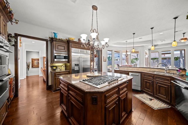 kitchen featuring a kitchen island, dark wood-type flooring, built in appliances, hanging light fixtures, and a sink