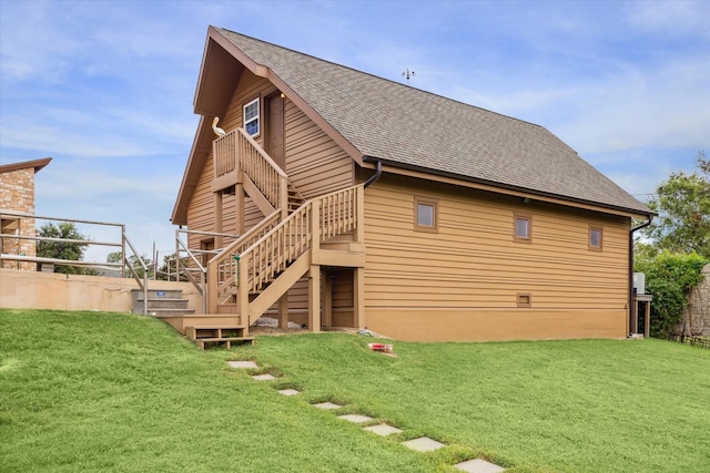 rear view of house featuring a shingled roof, a lawn, and stairway