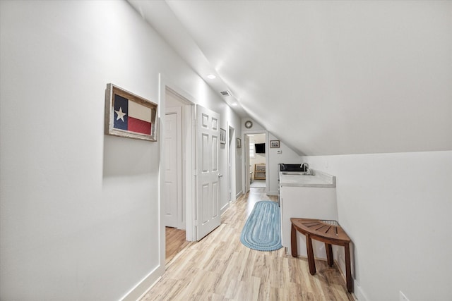 hallway featuring lofted ceiling, light wood finished floors, a sink, and baseboards