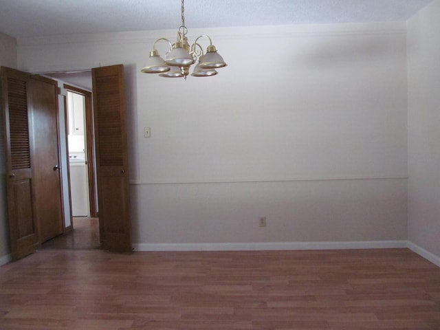 empty room featuring washer / clothes dryer, baseboards, light wood finished floors, and an inviting chandelier