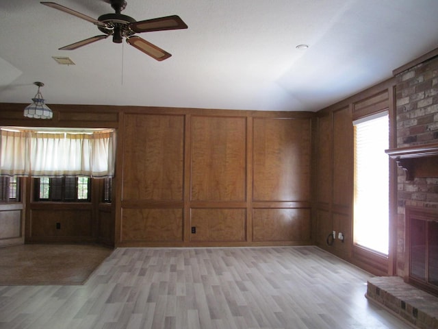 unfurnished living room featuring visible vents, vaulted ceiling, light wood-style floors, a fireplace, and a decorative wall