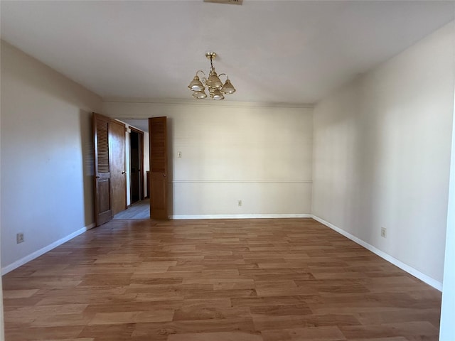 empty room featuring a chandelier, baseboards, visible vents, and light wood finished floors