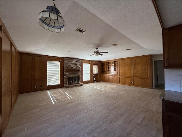 unfurnished living room featuring a textured ceiling, light wood-style flooring, a fireplace, and visible vents