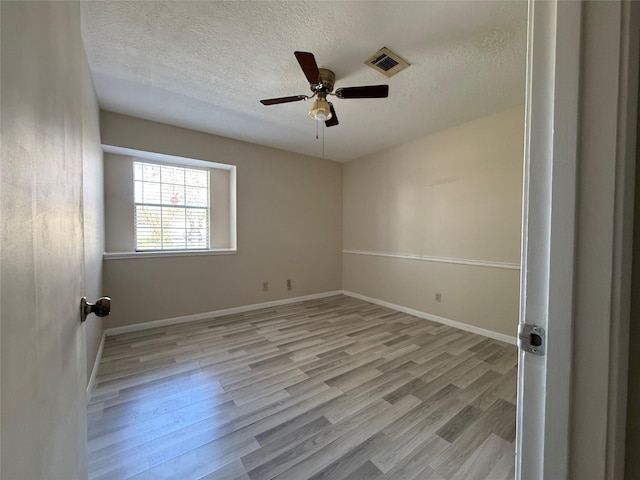 spare room featuring ceiling fan, a textured ceiling, visible vents, baseboards, and light wood-style floors