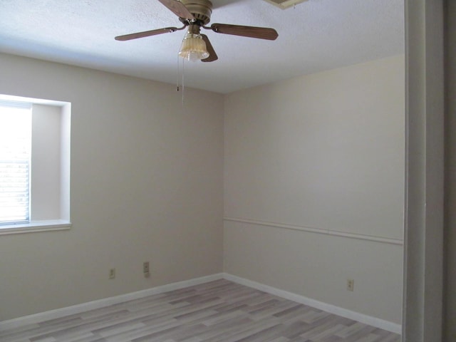 spare room with light wood-type flooring, ceiling fan, baseboards, and a textured ceiling