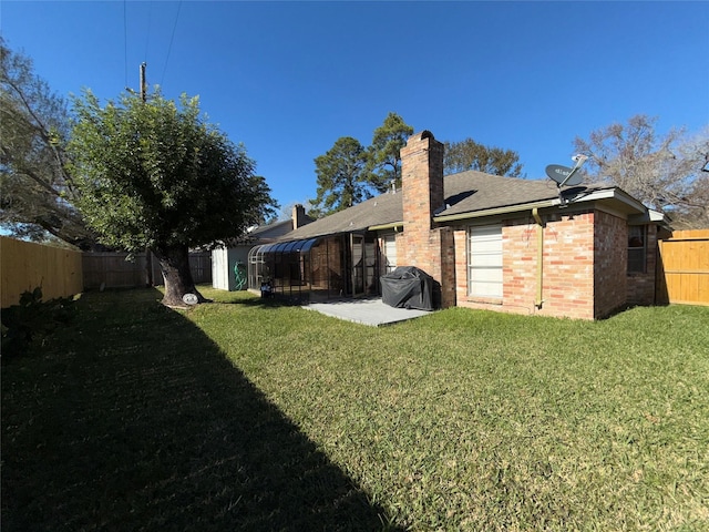 back of house with a yard, brick siding, a chimney, and a fenced backyard