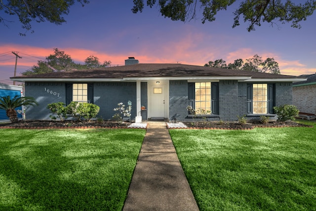 ranch-style home with brick siding, a lawn, and a chimney