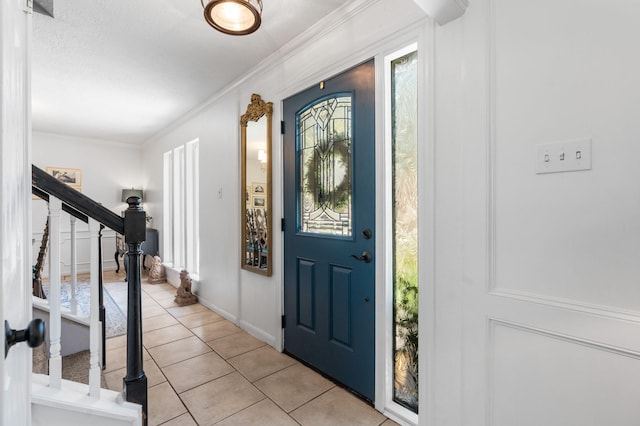 foyer with light tile patterned floors, stairway, baseboards, and crown molding