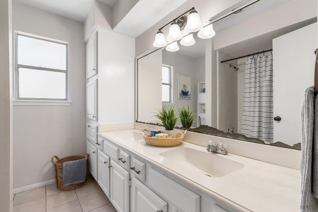 full bathroom with double vanity, curtained shower, a sink, tile patterned flooring, and baseboards