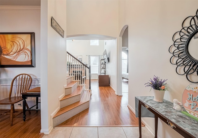 foyer featuring crown molding, baseboards, a towering ceiling, wood finished floors, and arched walkways