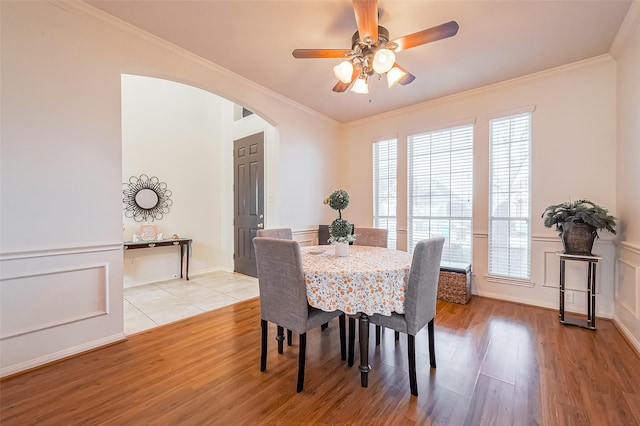 dining room with crown molding, a decorative wall, light wood-style floors, and arched walkways