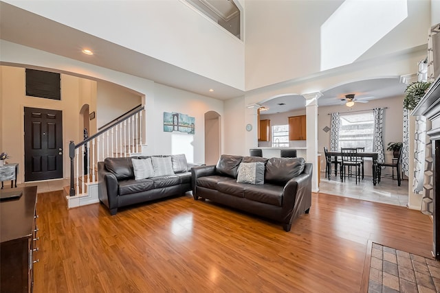 living room with light wood-style flooring, stairway, arched walkways, a high ceiling, and decorative columns