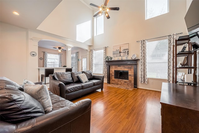 living area with decorative columns, arched walkways, ceiling fan, a tile fireplace, and light wood-type flooring