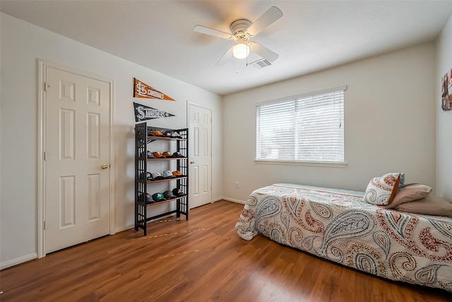 bedroom with ceiling fan, visible vents, baseboards, and wood finished floors