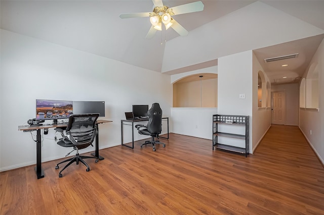 office area with visible vents, lofted ceiling, wood finished floors, arched walkways, and a ceiling fan