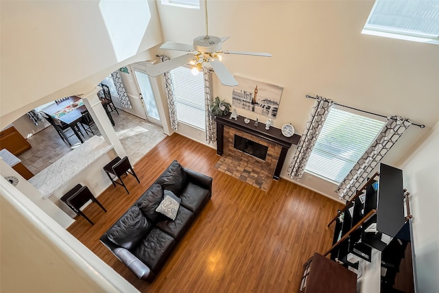 living area with a ceiling fan, wood finished floors, arched walkways, a high ceiling, and a tile fireplace