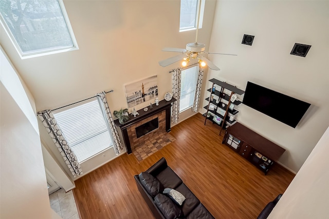 living area featuring a tiled fireplace, a high ceiling, wood finished floors, and a ceiling fan