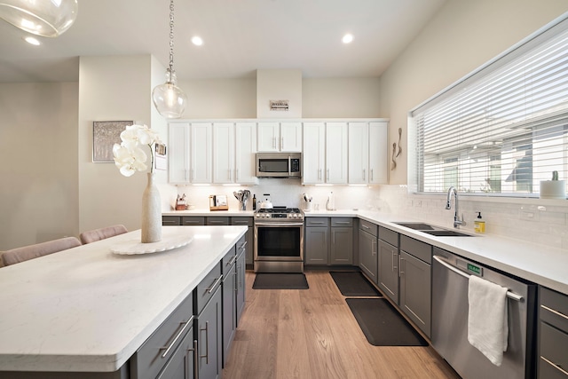 kitchen with tasteful backsplash, gray cabinetry, light wood-style flooring, appliances with stainless steel finishes, and a sink