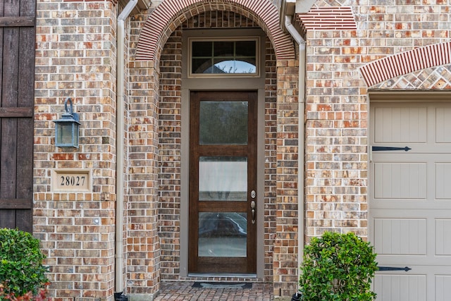 doorway to property featuring a garage and brick siding