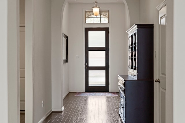 entryway with arched walkways, dark wood finished floors, and baseboards