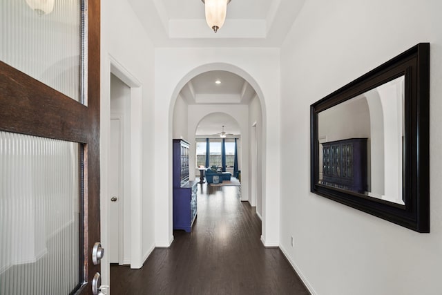 corridor featuring dark wood-style floors, a tray ceiling, and baseboards