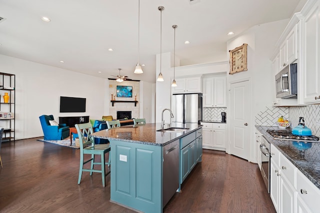 kitchen with stainless steel appliances, white cabinets, a fireplace, and a sink