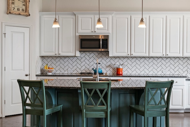 kitchen with tasteful backsplash, stainless steel microwave, and white cabinets