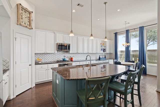 kitchen featuring dark wood finished floors, stainless steel microwave, dark stone countertops, white cabinetry, and a sink